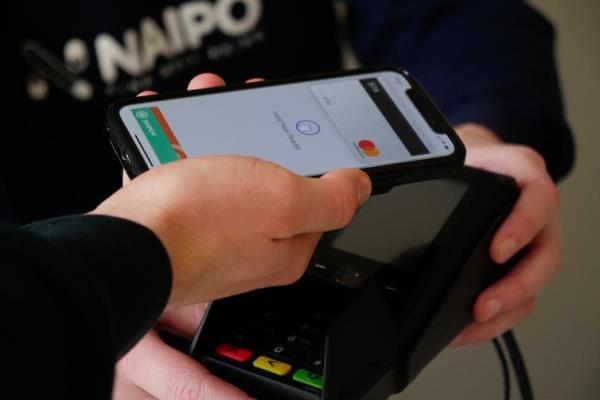 A person holding up their smartphone to a co<em></em>ntactless payment system
